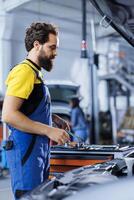 Serviceman in car service picks wrench from work station bench, using it to unscrew nuts in order to replace engine. Precise garage worker uses professional tools to fix customer automobile photo