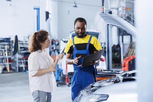 Mechanic in car service uses laptop to calculate invoice for client after repairing motor. Employee in garage with customer trying to determine final costs after servicing vehicle photo