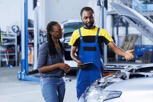 Mechanic in car service orders new compressor belt for damaged vehicle using tablet. Trained technician next to customer looking online for components to replace old ones in malfunctioning automobile photo
