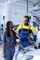 Mechanic in car service uses tablet to calculate invoice after fixing broken automobile motor. Certified auto repair shop worker uses device to inform woman of final costs after repairing vehicle photo