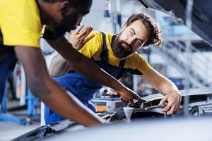 Colleagues in car service using professional mechanical tool to repair broken engine. Focused workers in garage repairing client automobile, ensuring optimal automotive performance, close up photo