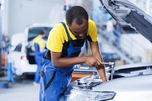 Engineer expertly examines car wheels using advanced mechanical tools, ensuring optimal automotive performance and safety. BIPOC trained garage employee conducts annual vehicle checkup photo