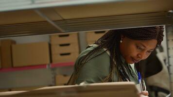 Close up shot of meticulous african american warehouse worker scanning cardboard boxes on shelves, updating merchandise labels info before sending parcels to be dispatched photo