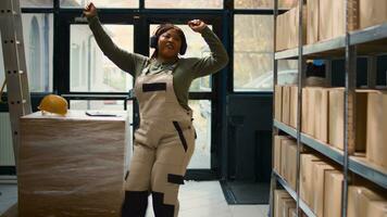 Chilled warehouse employee listening music enjoying herself while checking labels on cardboard boxes. Smiling worker wearing heaphones and dancing around while walking through storage hub rows photo