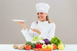 Female chef surrounded with vegetables holding plate. photo