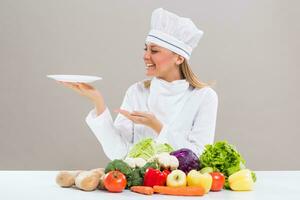 Female chef surrounded with vegetables holding plate. photo