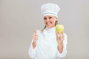 Beautiful female chef is showing thumb up and apple on gray background. photo