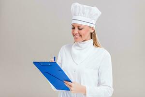 Beautiful female chef is holding cookbook and writing a new recipe. photo