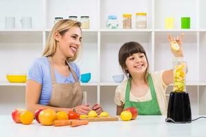 Happy mother and her daughter enjoy making smoothie together at their home. photo