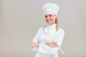 Portrait of beautiful female chef holding wooden spoon on gray background. photo