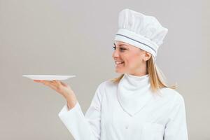 Beautiful female chef is holding plate on gray background. photo