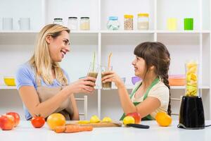 Happy mother and her daughter enjoy making and drinking smoothies together at their home. photo