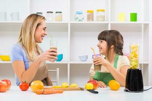 Happy mother and her daughter enjoy making and drinking smoothies together at their home. photo