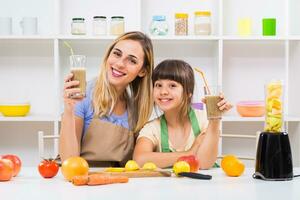 contento madre y su hija disfrutar haciendo y Bebiendo batidos juntos a su hogar. foto