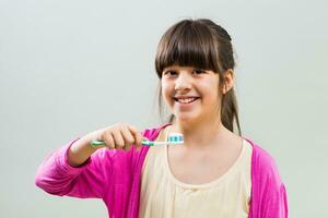 Little girl holding toothbrush on grey background photo