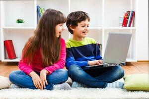 Two children sitting on the floor with a laptop photo