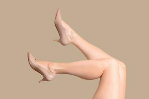 Womans legs in beige patent leather shoes hi heels isolated on beige nude background photo
