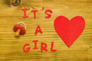 Text it's a girl with pacifier  and heart shape on wooden table photo