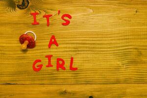 Text it's a girl with pacifier on wooden table photo