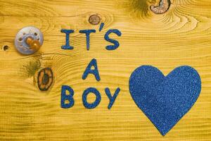 Text it's a boy with pacifier and  on wooden table photo