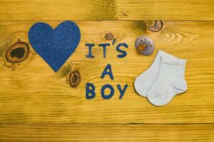 Text it's a boy with baby supplies and heart shape on wooden table photo