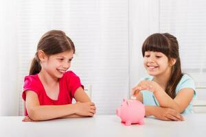 linda pequeño muchachas poniendo moneda dentro cerdito banco foto