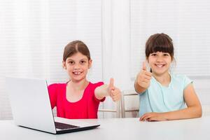 Cute little girls are sitting and using laptop. and showing thumbs up photo