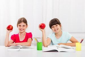 Cute little girls are having healthy snack while they are doing homework. photo