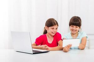 linda pequeño muchachas son sentado y utilizando ordenador portátil y digital tableta. foto