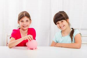 linda pequeño muchachas poniendo moneda dentro cerdito banco foto