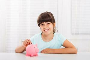 linda pequeño niña es poniendo moneda dentro cerdito banco foto