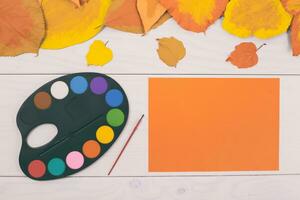 Autumn leaves and paint palette on white wooden background photo