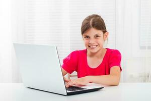 linda pequeño niña es utilizando ordenador portátil foto