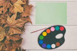 Autumn leaves and paint palette on a white wooden background photo