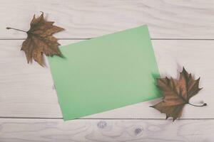 Autumn leaves and green paper on a wooden background photo