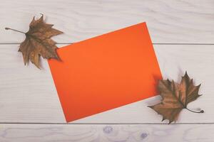 Autumn leaves and orange paper on wooden table photo