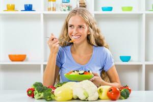 Beautiful girl enjoys eating vegetable salad at her home photo