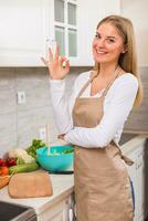 hermosa mujer demostración Okay firmar mientras haciendo comida en su cocina foto