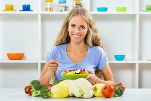 Beautiful girl enjoys eating vegetable salad at her home photo