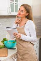 Beautiful woman reading cookbook while making a meal photo