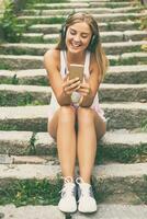 Beautiful young woman with headphones using mobile phone while sitting on the stairs in the city photo