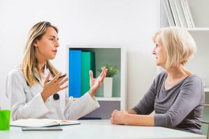 Female doctor and senior woman patient talking in doctor's office photo