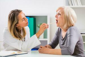 hembra médico examina su mayor del paciente garganta en oficina foto