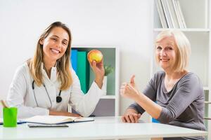 Female doctor is giving advice about eating healthy food to her senior woman patient photo