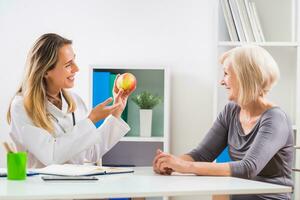 Female doctor is giving advice about eating healthy food to her senior woman patient photo
