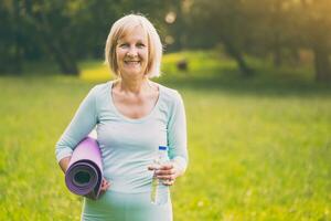 Portrait of sporty senior woman holding bottle of water and mat in the nature photo