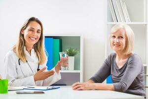 Female doctor is giving advice how is important to drink a lot of water to her senior woman patient photo