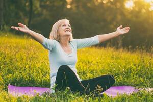 Senior woman enjoys sitting on the exercise mat with her arms outstretched in the nature photo
