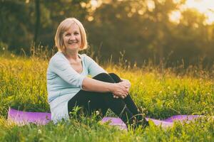 Portrait of sporty senior woman sitting on mat in the nature photo