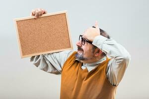 Nerdy businessman is in panic because of something while holding empty cork board photo